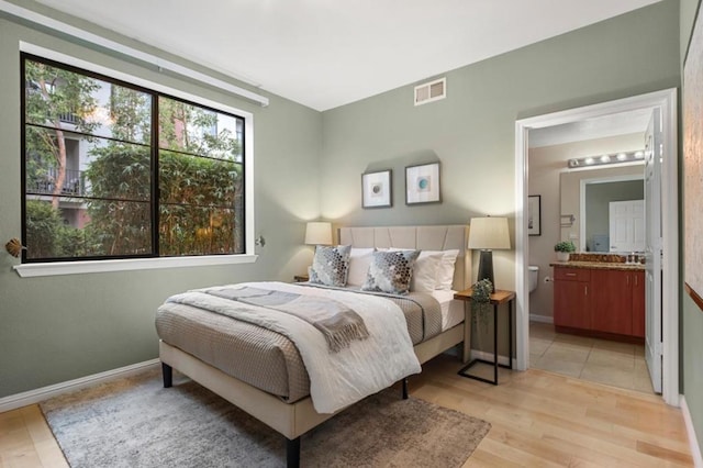 bedroom featuring connected bathroom and light hardwood / wood-style flooring