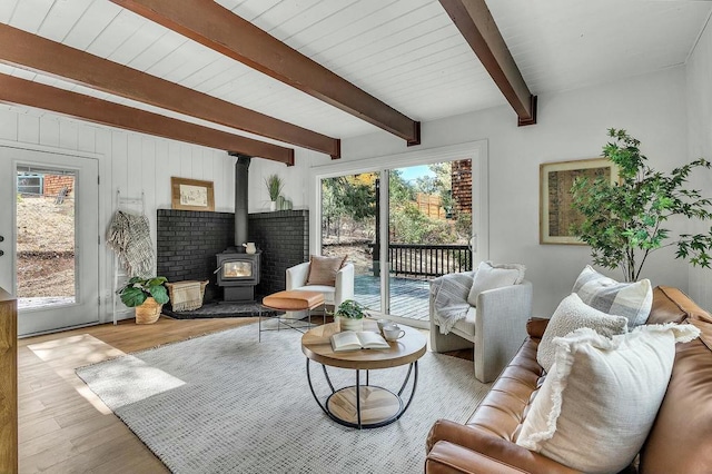 living room featuring a wood stove, beamed ceiling, a healthy amount of sunlight, and light wood-type flooring