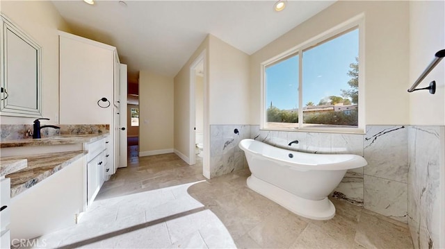 bathroom featuring a tub to relax in, vanity, and tile walls