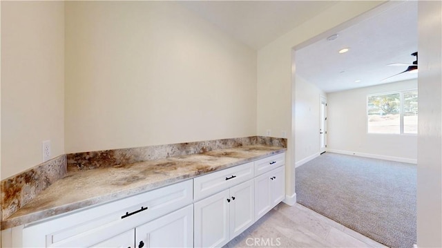 interior space with light stone countertops, ceiling fan, light colored carpet, and white cabinetry