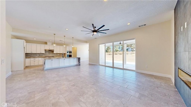 kitchen with pendant lighting, a tile fireplace, a center island with sink, white cabinets, and ceiling fan