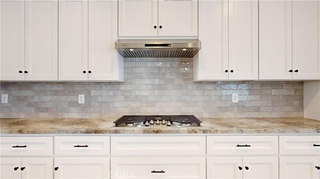 kitchen featuring stainless steel gas stovetop, wall chimney range hood, tasteful backsplash, light stone counters, and white cabinetry