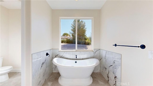 bathroom with tile patterned flooring, a bathtub, toilet, and tile walls