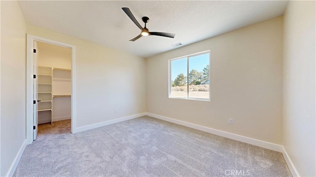 unfurnished bedroom featuring ceiling fan, a walk in closet, light carpet, and a closet