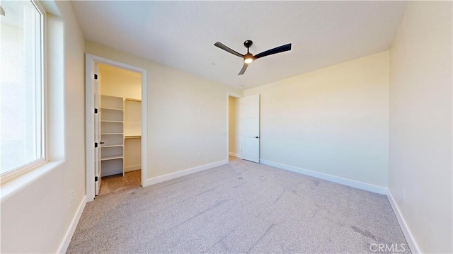 unfurnished bedroom with a walk in closet, ceiling fan, a closet, and light carpet