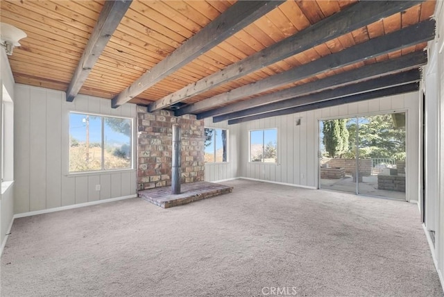 unfurnished living room featuring beamed ceiling, carpet flooring, a wood stove, and wooden ceiling