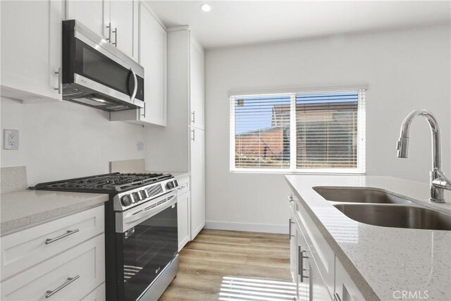 kitchen featuring white cabinets, stainless steel appliances, light stone countertops, and sink