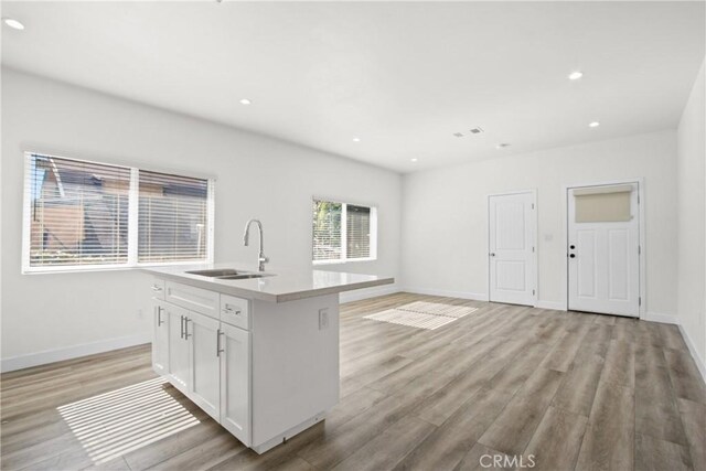 kitchen with white cabinetry, a kitchen island with sink, sink, and light hardwood / wood-style flooring