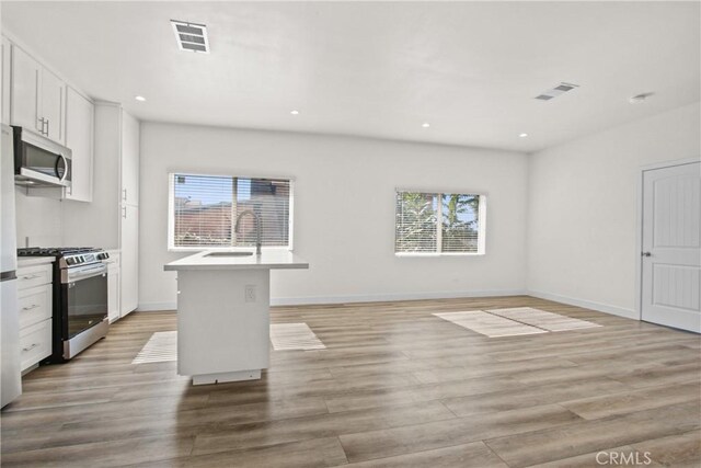 kitchen with white cabinets, sink, stainless steel appliances, and a kitchen island with sink