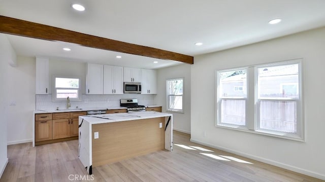 kitchen with sink, beam ceiling, stainless steel appliances, white cabinets, and a kitchen island