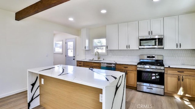 kitchen featuring sink, beam ceiling, stainless steel appliances, a center island, and white cabinets