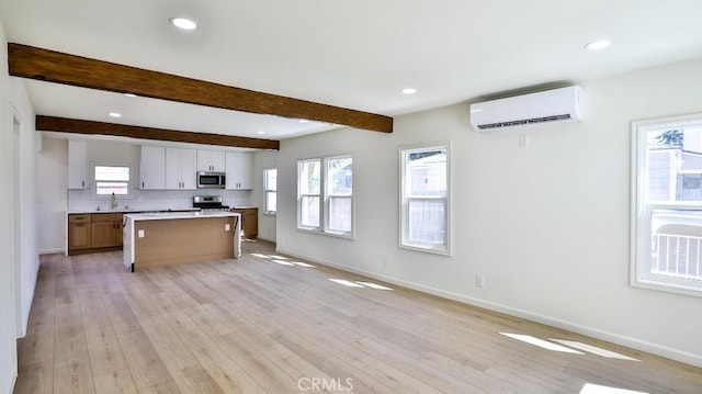 kitchen featuring white cabinetry, a center island, a wall unit AC, beamed ceiling, and stainless steel appliances