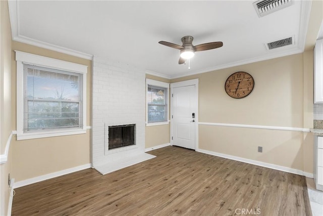 unfurnished living room with a brick fireplace, ceiling fan, wood-type flooring, and ornamental molding