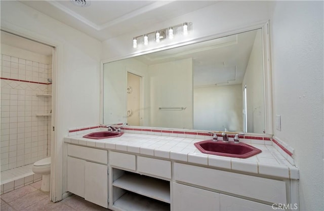 bathroom with tile patterned flooring, vanity, tiled shower, and toilet