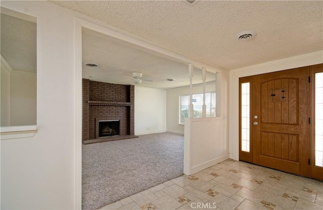 entrance foyer with a textured ceiling, a fireplace, ceiling fan, and light carpet