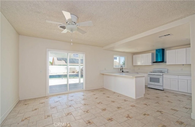 kitchen featuring white range, wall chimney range hood, kitchen peninsula, a textured ceiling, and white cabinetry