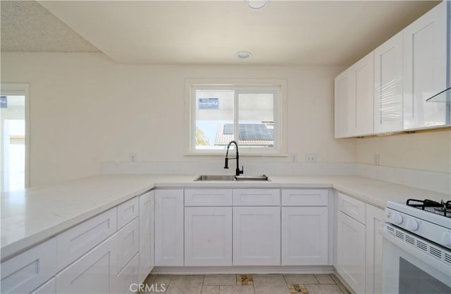 kitchen with light stone countertops, sink, white range, kitchen peninsula, and white cabinets