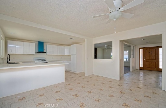 kitchen with kitchen peninsula, white range oven, sink, wall chimney range hood, and white cabinetry