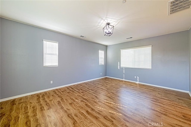 unfurnished room featuring wood-type flooring, a wealth of natural light, and an inviting chandelier