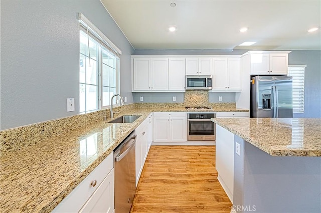 kitchen with appliances with stainless steel finishes, light stone counters, sink, white cabinets, and light hardwood / wood-style floors