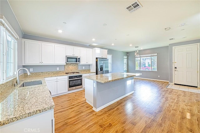 kitchen with sink, light hardwood / wood-style flooring, a kitchen island, white cabinetry, and stainless steel appliances