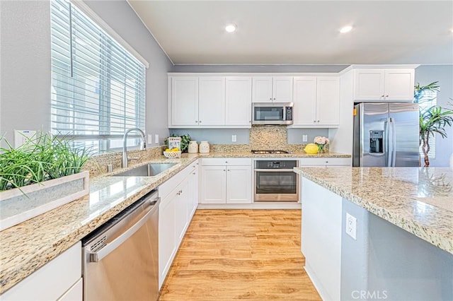 kitchen with sink, light wood-type flooring, white cabinetry, stainless steel appliances, and light stone countertops