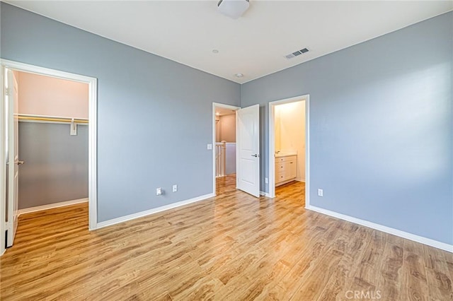 unfurnished bedroom with light wood-type flooring, a closet, ensuite bath, and a spacious closet