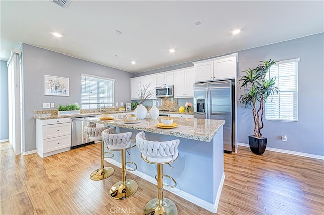 kitchen featuring a center island, appliances with stainless steel finishes, white cabinetry, and light hardwood / wood-style flooring