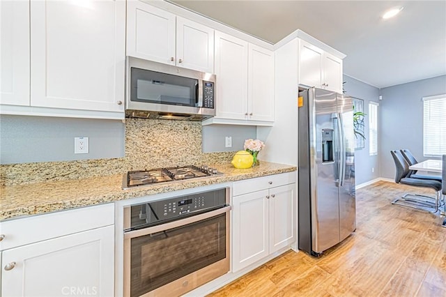 kitchen featuring stainless steel appliances, light hardwood / wood-style floors, tasteful backsplash, light stone counters, and white cabinets