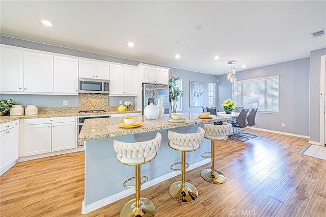 kitchen featuring a kitchen bar, appliances with stainless steel finishes, white cabinetry, and light hardwood / wood-style flooring