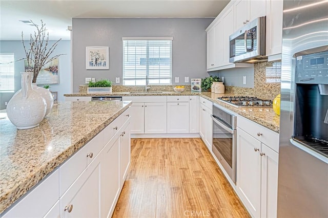 kitchen with appliances with stainless steel finishes, light wood-type flooring, light stone counters, white cabinets, and sink