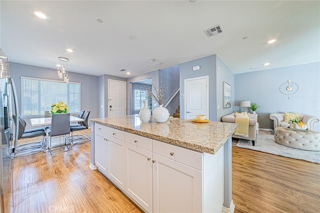 kitchen with white cabinetry, a center island, light stone counters, and light hardwood / wood-style flooring