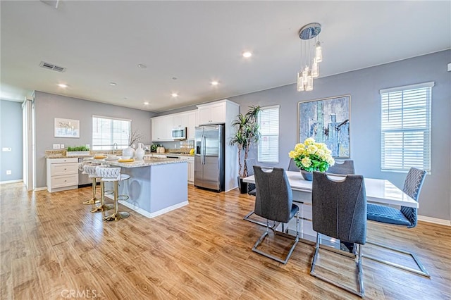 kitchen featuring a center island, white cabinetry, stainless steel appliances, hanging light fixtures, and light stone countertops