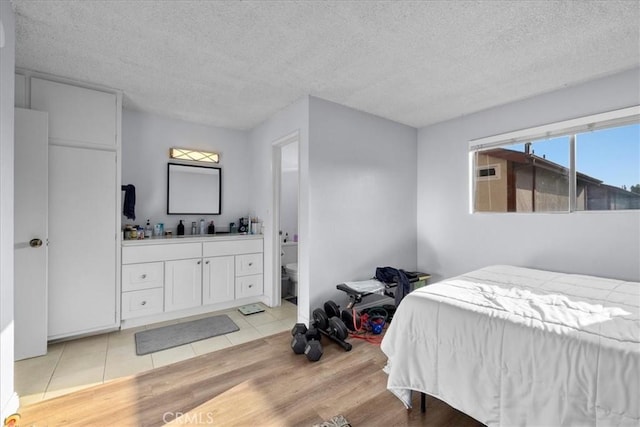 bedroom with connected bathroom, light hardwood / wood-style floors, and a textured ceiling