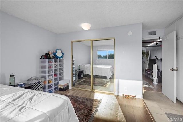 bedroom with light hardwood / wood-style floors, a textured ceiling, and a closet