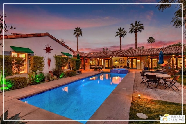 pool at dusk with an in ground hot tub and a patio area