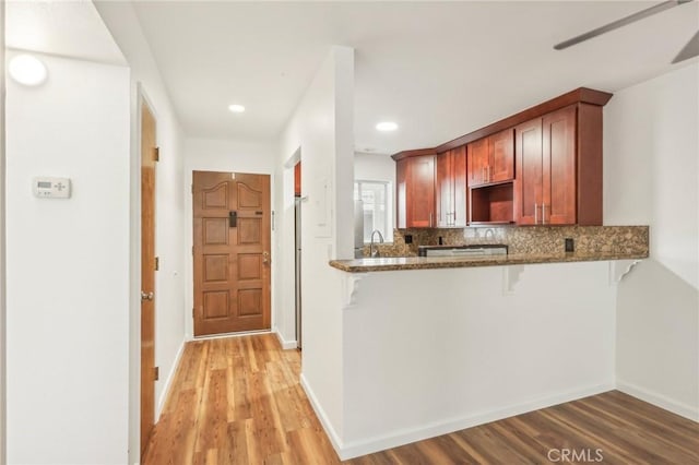 kitchen with tasteful backsplash, dark stone countertops, kitchen peninsula, sink, and light hardwood / wood-style flooring