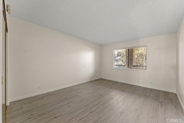 empty room with a textured ceiling and light hardwood / wood-style flooring