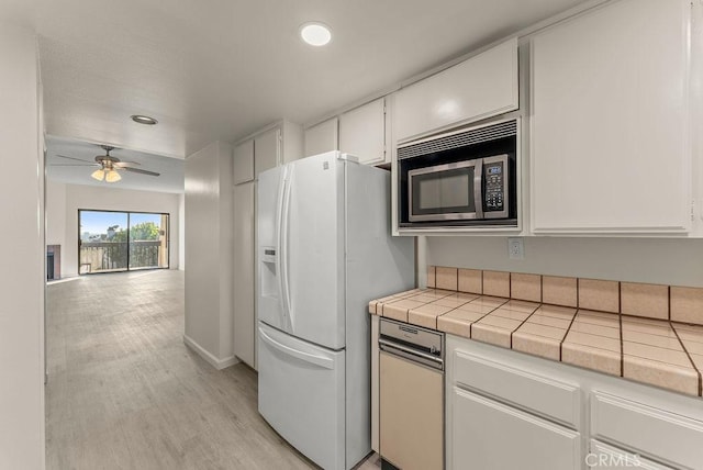 kitchen featuring ceiling fan, white refrigerator with ice dispenser, tile countertops, white cabinets, and light wood-type flooring