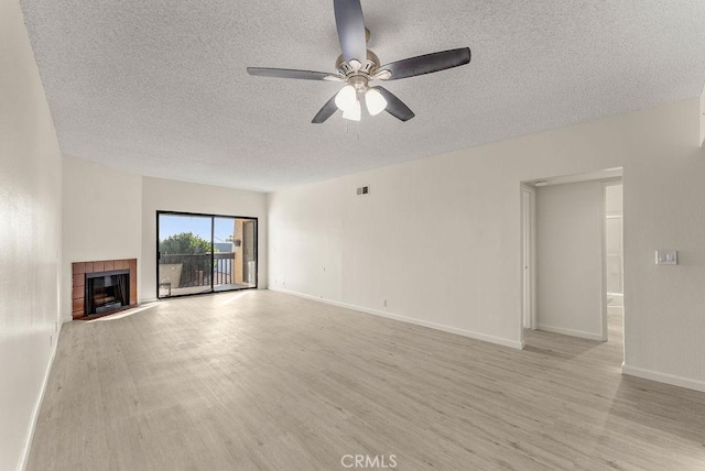 unfurnished living room with a tile fireplace, a textured ceiling, light hardwood / wood-style flooring, and ceiling fan