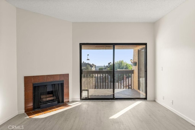 unfurnished living room with a tiled fireplace, hardwood / wood-style floors, and a textured ceiling