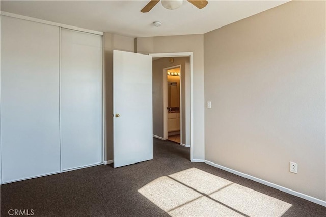 unfurnished bedroom with ceiling fan, dark carpet, and a closet