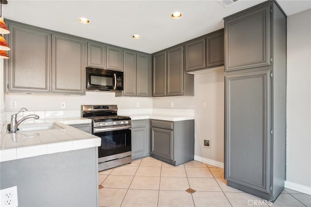 kitchen featuring sink, stainless steel gas range oven, tile countertops, gray cabinets, and light tile patterned floors