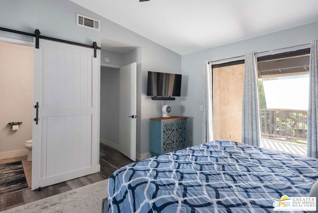 bedroom with dark wood-type flooring, a barn door, ensuite bathroom, and lofted ceiling