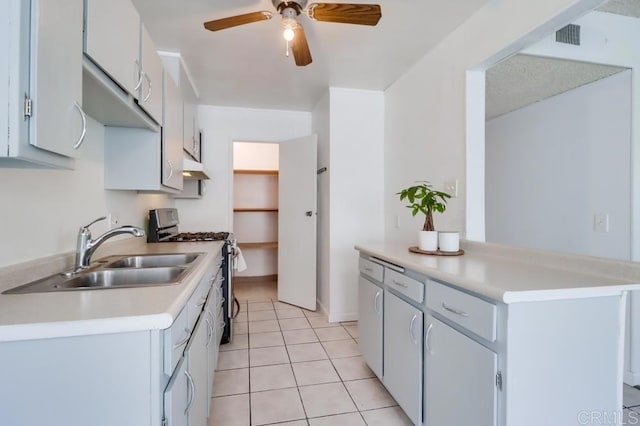 kitchen with ceiling fan, sink, stainless steel range with gas stovetop, white cabinets, and light tile patterned floors