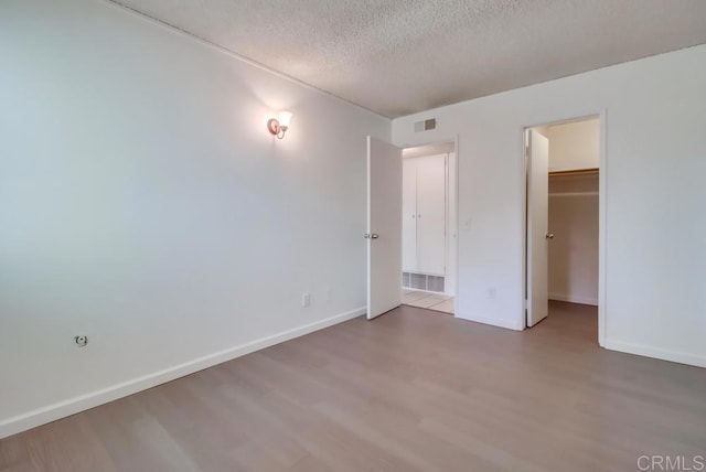 unfurnished bedroom featuring a closet, wood-type flooring, a spacious closet, and a textured ceiling