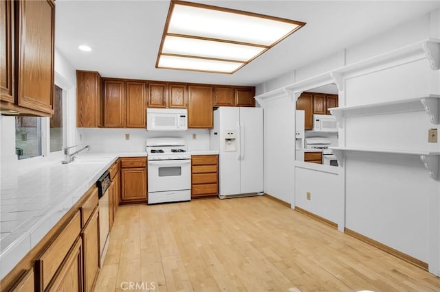 kitchen with light wood-type flooring, white appliances, tile counters, and sink