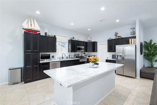 kitchen with light stone countertops, a center island, stainless steel appliances, and sink