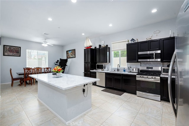 kitchen featuring ceiling fan, sink, light stone countertops, a kitchen island, and appliances with stainless steel finishes