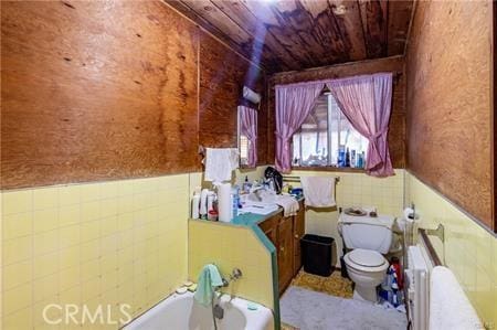 bathroom featuring radiator, toilet, a bathtub, wood ceiling, and tile walls